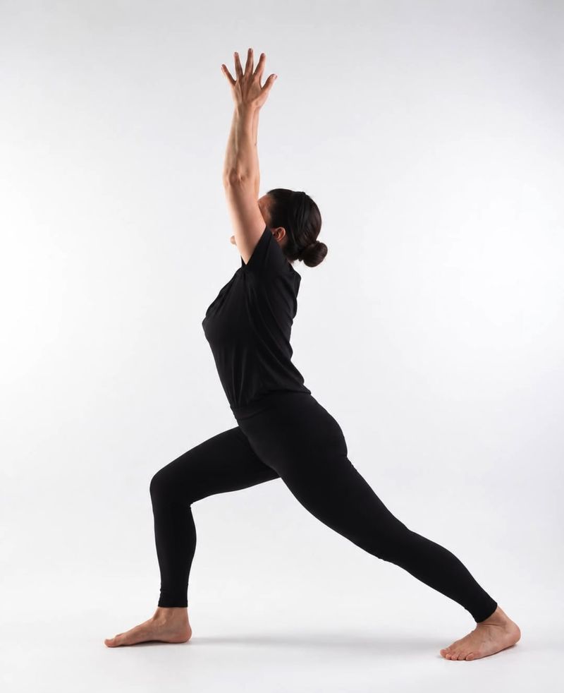 Alice in a high lunge with her arms stretched up, in a bright studio